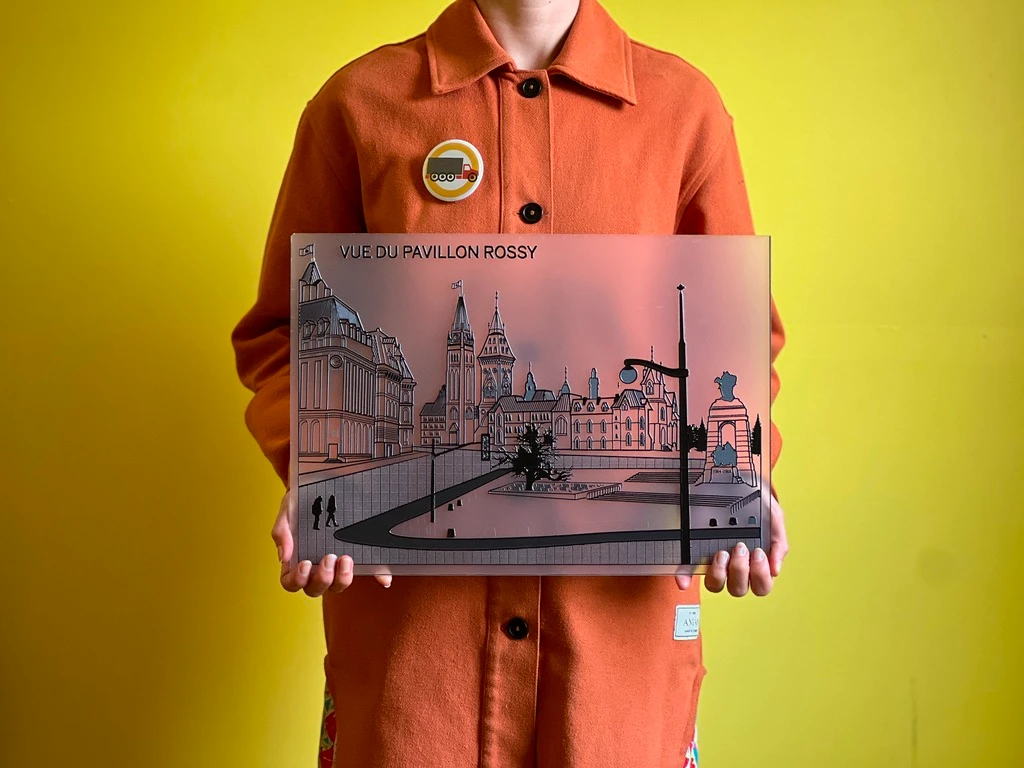 A person in an orange coat holds a raised-line embossed print titled “Vue du Pavillon Rossy,” showing a grand building and plaza rendered as touchable relief lines.